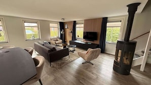 A modern living room with a sofa, armchairs, a TV, a fireplace, and large windows.