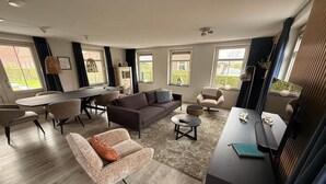 A modern living room with a sofa, chairs, a dining table, and a TV stand.