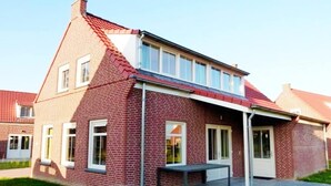 A two-story brick house with a red roof, a covered porch, and a small patio.