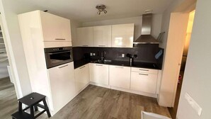 A compact kitchen with white cabinets, a black countertop, and a small stool.