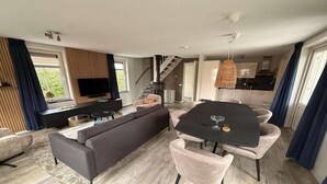 A modern living room with a sofa, dining table, and chairs, a staircase, and a kitchen area.