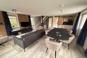 Un saló modern amb un sofà, taula de dinar i cadires, una escala i una zona de cuina.
