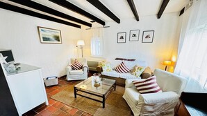 A living room with a white sofa, a white armchair, a glass coffee table, and a white desk with a lamp.