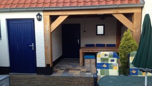 A covered outdoor seating area with a wooden bench, a small table, and a green umbrella. - Historic Cottage w/ Garden (Breskens)
