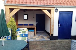 A covered outdoor seating area with a checkered floor, a wooden bench, and a table.