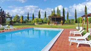 Ein rechteckiger Pool mit einer Fliesenverkleidung, umgeben von einer Ziegelterrasse. Im Hintergrund sind weiße Liegestühle und eine Pergola zu sehen.