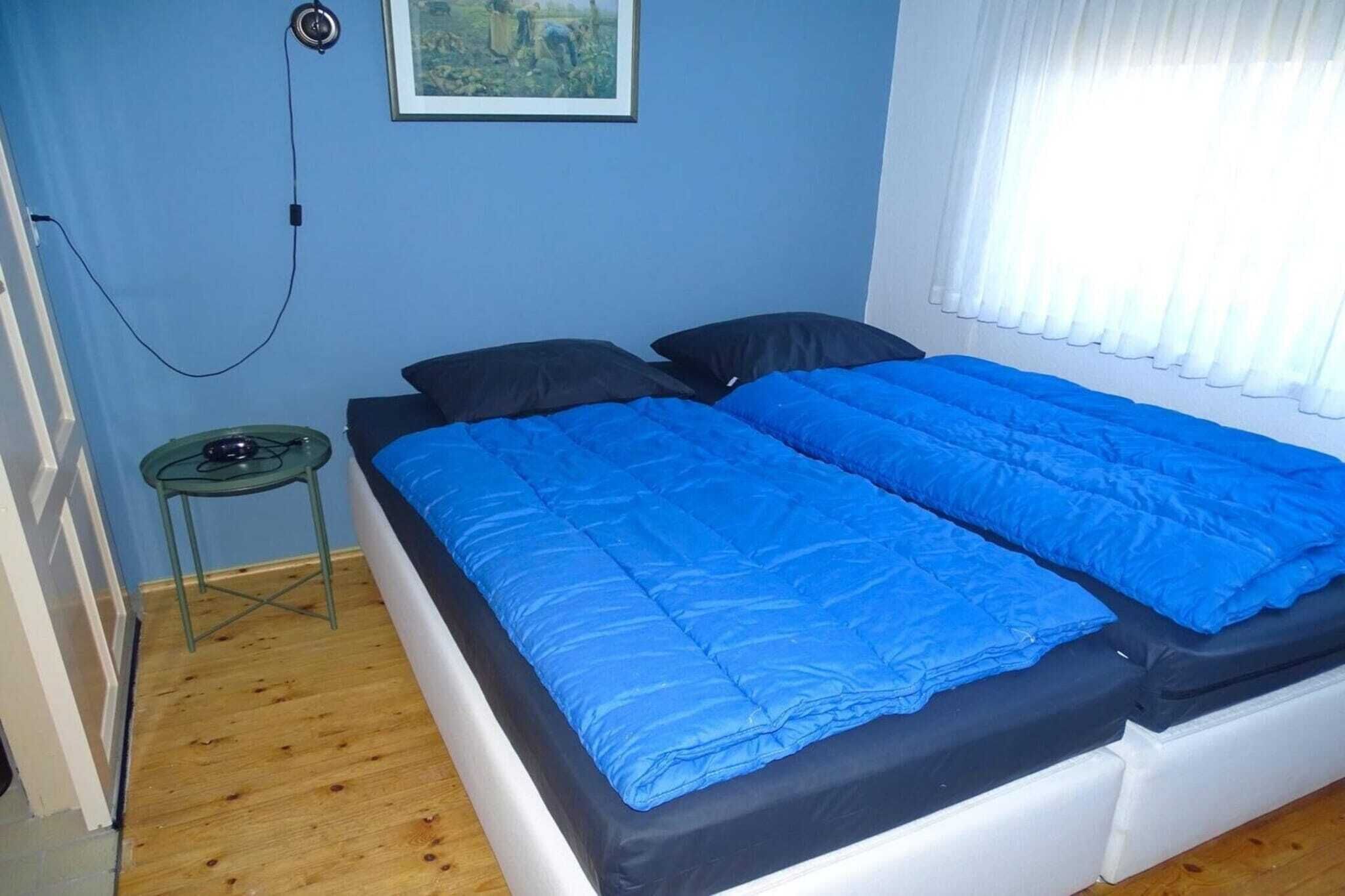 Ein Zimmer mit einem Bett, einem kleinen Tisch, einer Steckdose und einem Fenster mit Vorhängen.