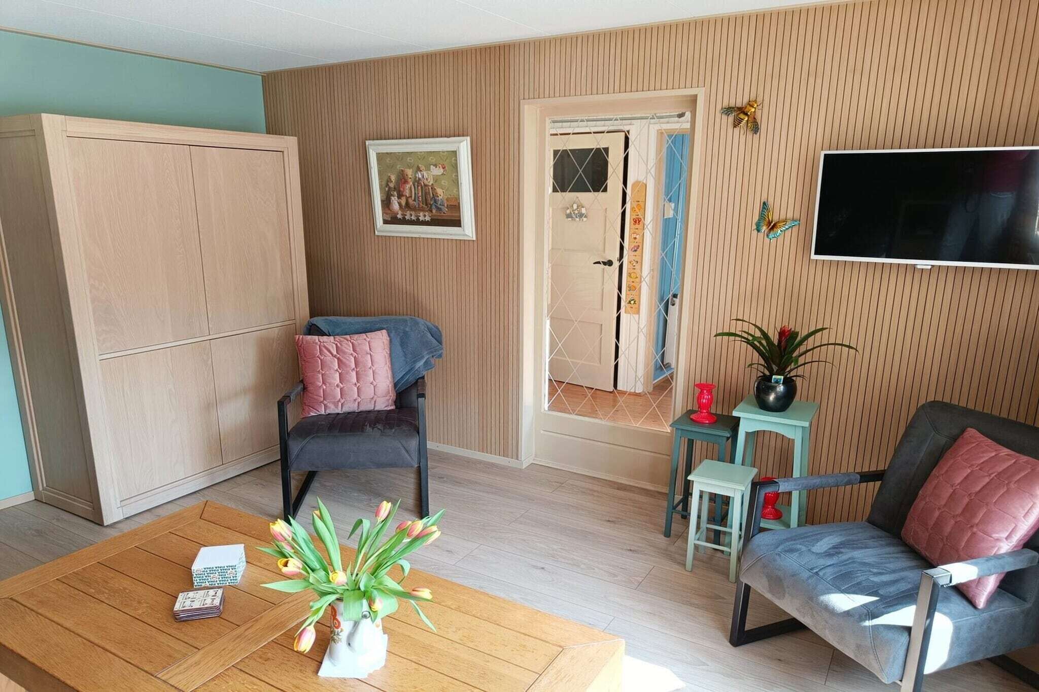 A living room with a sofa, a chair, a coffee table, a TV, a wardrobe, a door, and a wall-mounted TV.