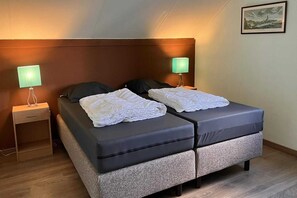 Una cama doble con cabecera, dos mesitas de noche con lámparas, un cuadro enmarcado en la pared y una pequeña mesita de madera.