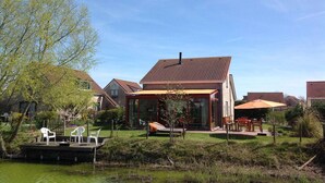 A house with a large glass extension, a deck with chairs, and a pond in the yard. - Pet-Friendly Coastal Home (Breskens)