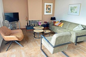 Uma sala de estar com sofá, poltrona, televisão, lareira e obras de arte.