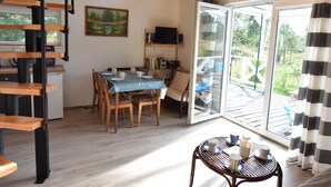 A dining area with a table set for four, a television on a shelf, and a view of the outdoors through a glass door. - Holiday Home Near Lake Mausz With Sauna (Parchowo)