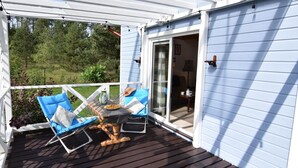A covered deck with two blue cushioned chairs and a small table, a white railing, and a view of a green landscape. - Holiday Home Near Lake Mausz With Sauna (Parchowo)
