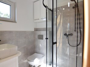 Bathroom features a glass-enclosed shower, handheld showerhead, and wall-mounted faucet.