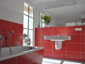Un baño moderno con una bañera blanca, paredes de baldosas rojas y una ventana con vistas al exterior.