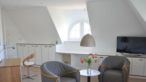 Ett modernt sovrum i loftstil med ett sluttande tak, en matplats med bord och stolar samt en tv som står på ett stativ.