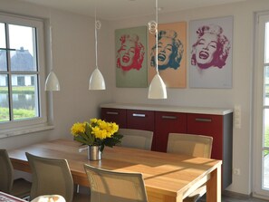 Un comedor con una mesa de madera, sillas, un jarrón de flores amarillas y tres lámparas colgantes en la pared.