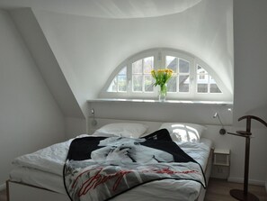 Un dormitorio con una cama, una ventana con vistas y un jarrón con flores.