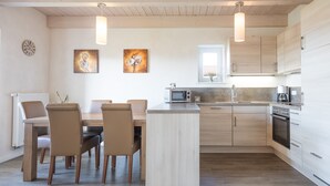 A modern kitchen with wooden cabinets, a central island, and a dining area with chairs. - Exklusiv Eingerichtetes Ferienhaus in Strandnahe (Dagebuell)