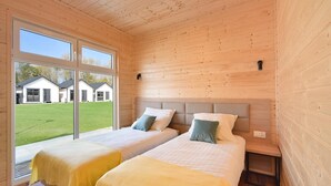 A room with two beds, a large window, and a view of houses outside.