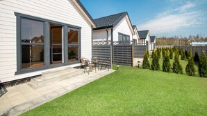 A modern house with large windows, a patio with outdoor furniture, and a well-maintained lawn.