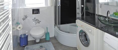 A compact bathroom with a glass-enclosed shower, a white toilet, a washing machine, and a sink with a glass basin.