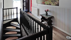 A staircase with a black railing, a small table with a vase of flowers, and a large window with a view of a building and garden.