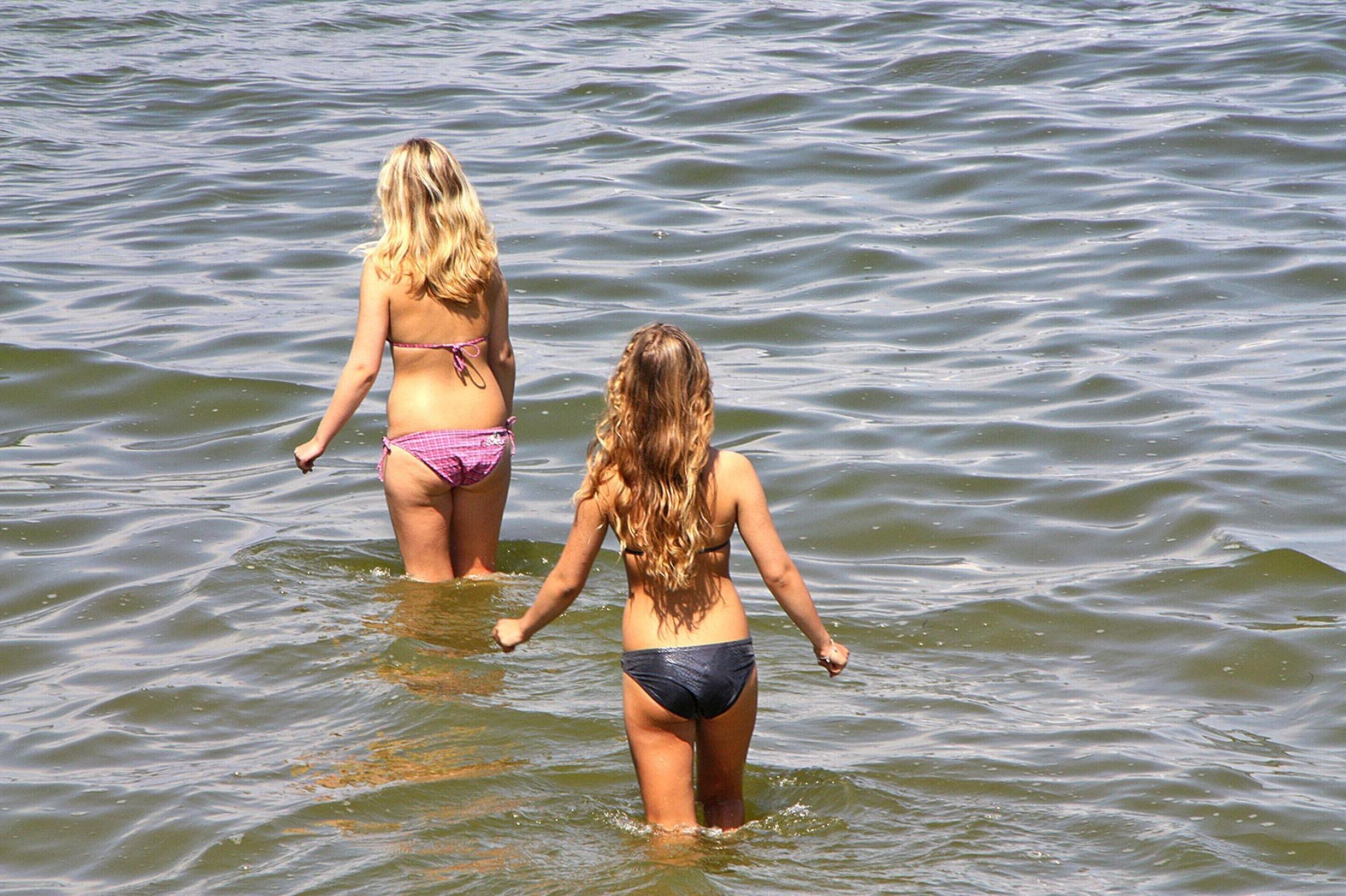 Two individuals in a body of water, wearing bikinis.