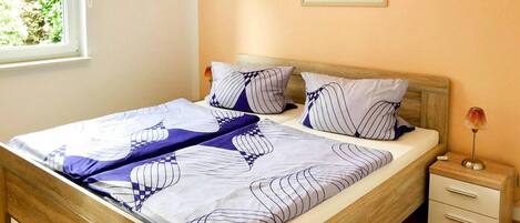 A neatly made bed with striped bedding, a wooden headboard, and a nightstand with a lamp.