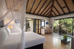 Relax in a serene space with a large bed, glass coffee table, and desk area, surrounded by lush greenery views.