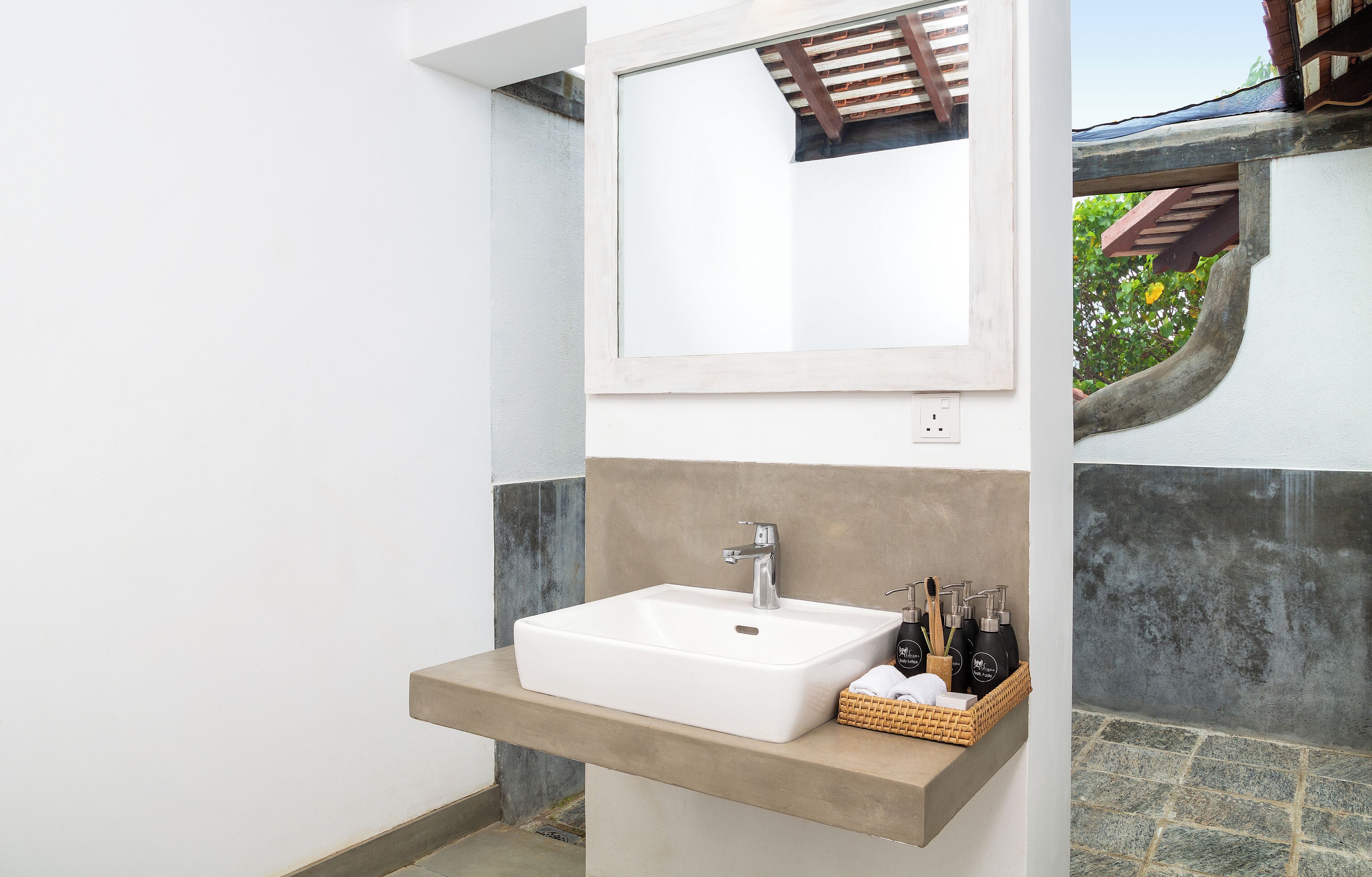 Une salle de bain avec un lavabo blanc, un miroir et une étagère contenant des articles de toilette.