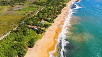 Imóvel costeiro com praia, piscina e vegetação ao redor.