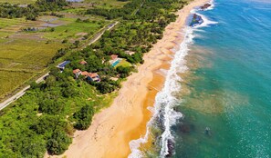 Una propiedad costera con playa, piscina y vegetación circundante.
