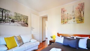 A hotel room with a white sofa, a bed with dark bedding, and two paintings depicting Parisian scenes. - Comfortable 3-room Apartment Close to the sea (Ustronie Morskie)