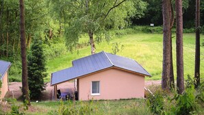 A small, single-story building with a sloped roof, surrounded by dense greenery and trees. - Bungalows am Vordersee, Dobbrikow (Nuthe-Urstromtal)