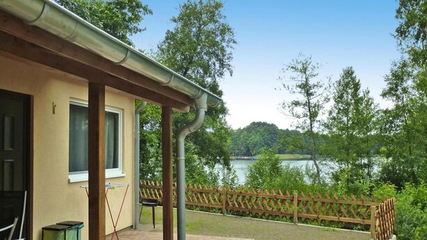 A patio with a brick floor, a wooden fence, and a view of a lake. - Bungalows am Vordersee, Dobbrikow (Nuthe-Urstromtal)