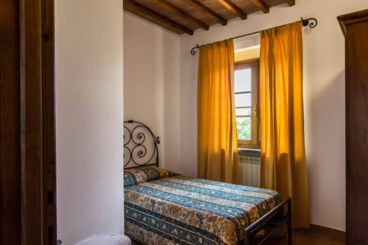 A bedroom with a bed, a window with yellow curtains, a wooden wardrobe, and a radiator.