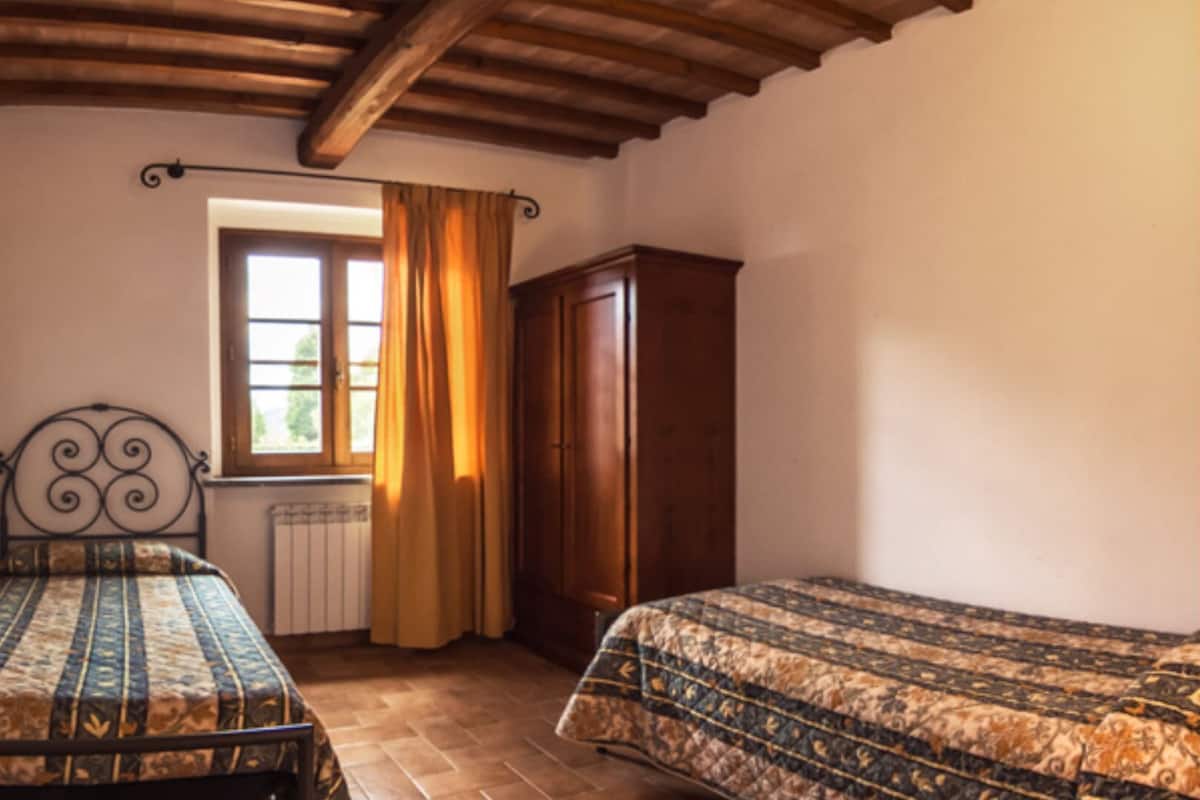 A bedroom with two beds, a window with curtains, a radiator, and a wardrobe.