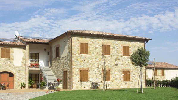 A stone building with a balcony, a staircase, and a small garden area. - Il Casino (Lajatico)