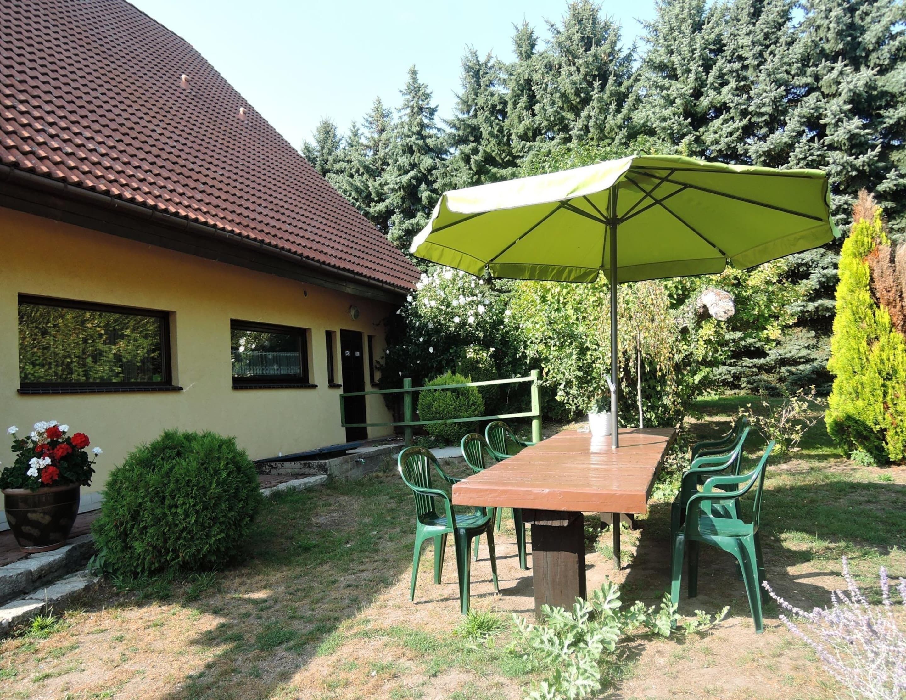 Une terrasse avec une table et des chaises, un parasol vert et une maison avec un toit en tuiles.