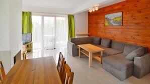 A modern living room with a wooden dining table, grey sofa, and a painting on the wooden wall. - Spacious Holiday Home With Private Garden (Mielno)