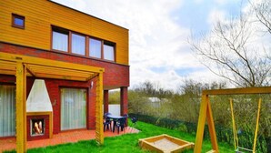 A modern two-story house with a brick facade, a wooden pergola, a barbecue area, and a swing set in the backyard. - Spacious Holiday Home With Private Garden (Mielno)