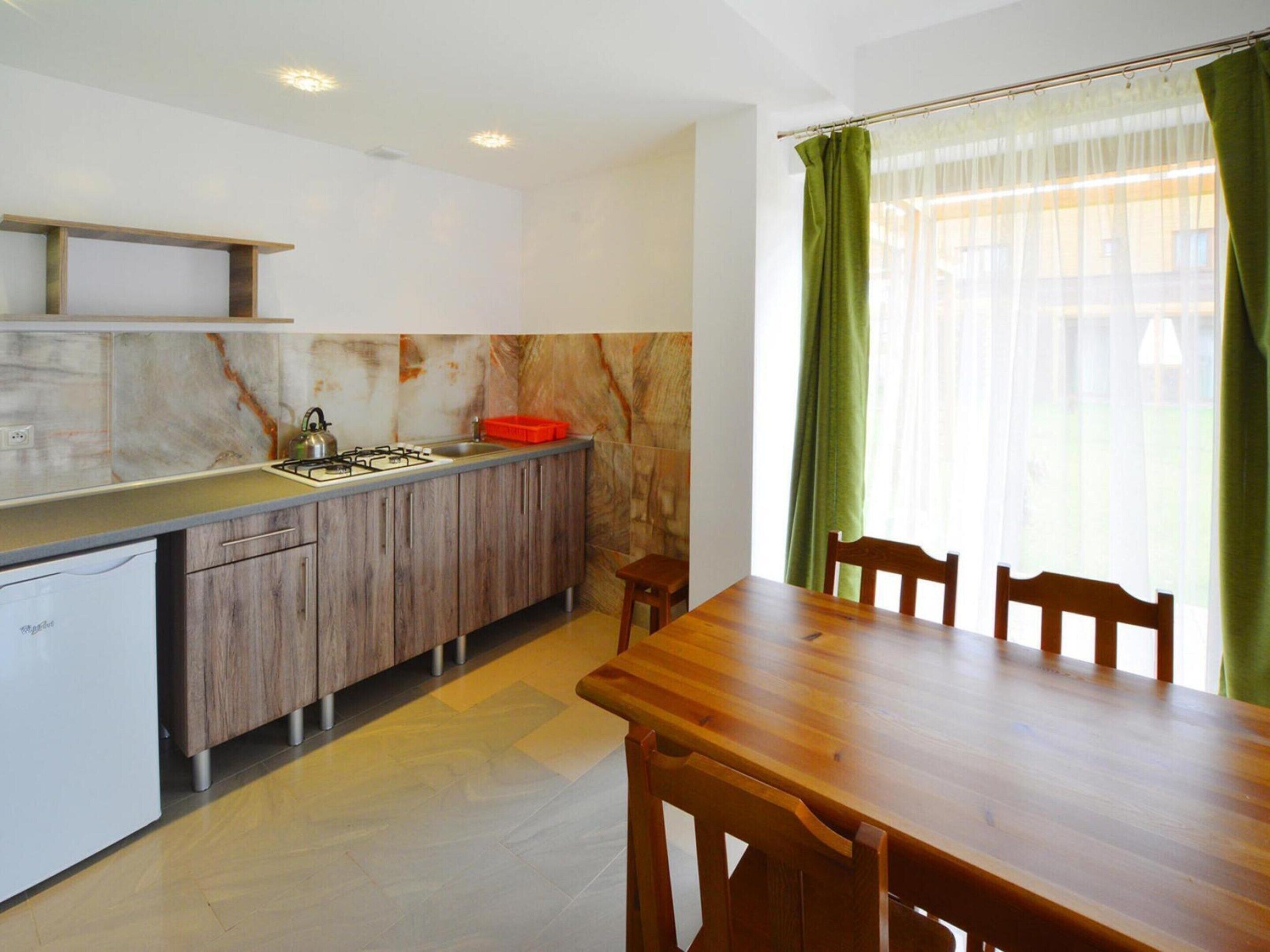 A modern kitchen with a marble backsplash, wooden cabinets, and a dining area with a wooden table and chairs.