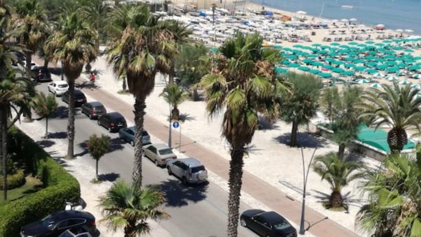 A beachside road lined with palm trees, a parking area, and a beach with umbrellas and sun loungers. - Apartment in Pietra Ligure (Pietra Ligure)