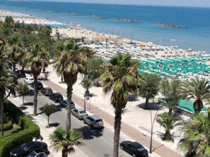 A beachside road lined with palm trees, a parking area, and a beach with umbrellas and sun loungers. - Apartment in Pietra Ligure (Pietra Ligure)