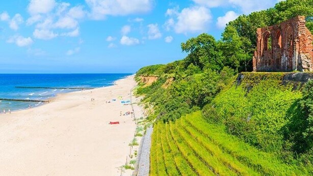 Une plage avec un bâtiment historique situé sur une falaise.