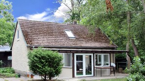 Ein eingeschossiges Haus mit Ziegeldach, einer überdachten Terrasse und einem kleinen Garten.