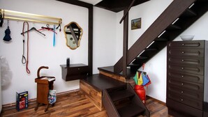 Ein Zimmer mit Holzboden, einer dunklen Treppe, einem Spiegel, einem Kleiderständer und einem kleinen Holztisch.