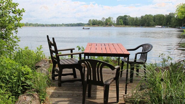 Eine Holzterrasse mit Tisch und Stühlen mit Blick auf einen See.