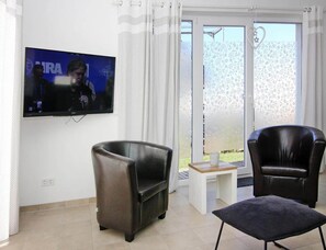 A living room with a flat-screen TV mounted on the wall, two leather armchairs, a small wooden table, and a sliding glass door leading to an outdoor area. - Ferienhaus, Boiensdorf (Boiensdorf)